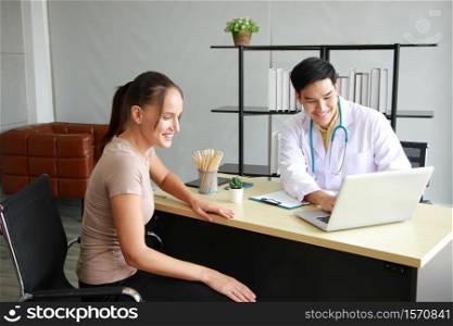 Young Asian male psychiatrist is specialist in psychiatry Caucasain female Patient is smiling together for therapy and talking for encourage with laptop in Clinical treatment for emotional symptoms.