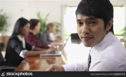 Young Asian man at work as manager in business meeting and smiling at camera. Rack focus