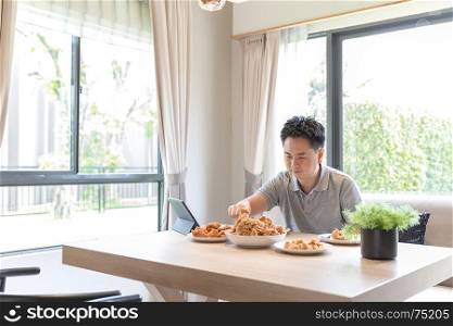 Young Asian man eating fried chicken in living room of contemporary house for modern lifestyle concept