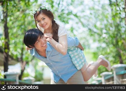Young asian man giving a piggy back to his girlfriend in the park