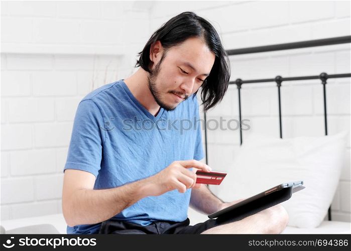 Young asian man holding credit card and using digital tablet for shopping on line at home, business and technology concept, digital marketing, casual lifestyle