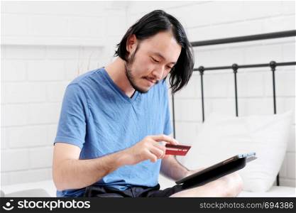 Young asian man holding credit card and using digital tablet for shopping on line at home, business and technology concept, digital marketing, casual lifestyle