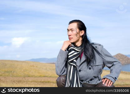 Young asian man in grey coat and striped black-and-white scarf. The tracery on his cheek is his name Chinghis in ancient Mongolian.