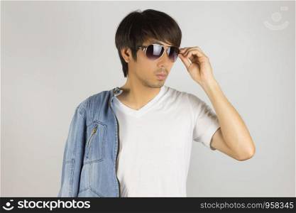 Young Asian Man in Jeans Jacket or Denim Jacket Touching Sunglasses and Show White T-Shirt. Denim or Jeans Jacket Men Fashion on Gray Background