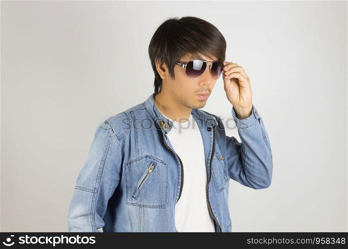 Young Asian Man in Jeans Jacket or Denim Jacket Touching Sunglasses in 45 Degree View. Denim or Jeans Jacket Men Fashion on Gray Background