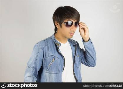 Young Asian Man in Jeans Jacket or Denim Jacket Touching Sunglasses in 45 Degree View. Denim or Jeans Jacket Men Fashion on Gray Background