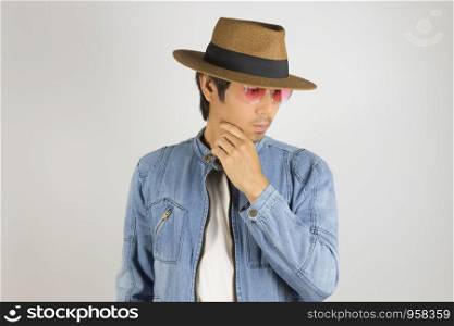 Young Asian Man in Jeans Jacket or Denim Jacket Wear Red Glasses and Hat Touching Chin Pose. Denim or Jeans Jacket Men Fashion on Gray Background