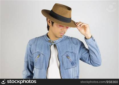 Young Asian Man in Jeans Jacket or Denim Jacket Wear Red Glasses and Touch Hat Brim and Looking Below. Denim or Jeans Jacket Men Fashion on Gray Background