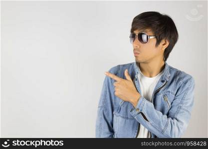 Young Asian Man in Jeans Jacket or Denim Jacket Wear Sunglasses and Pointing Finger. Denim or Jeans Jacket Men Fashion on Gray Background