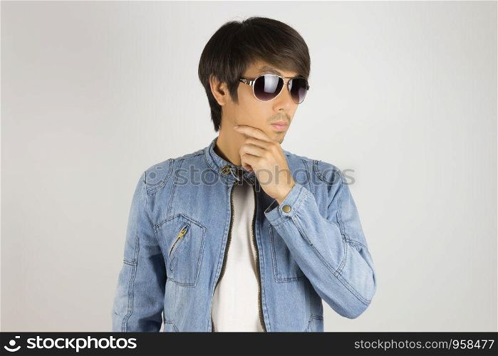 Young Asian Man in Jeans Jacket or Denim Jacket Wear Sunglasses and Touch Chin Pose. Denim or Jeans Jacket Men Fashion on Gray Background