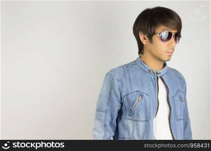 Young Asian Man in Jeans Jacket or Denim Jacket Wear Sunglasses at Right Frame. Denim or Jeans Jacket Men Fashion on Gray Background