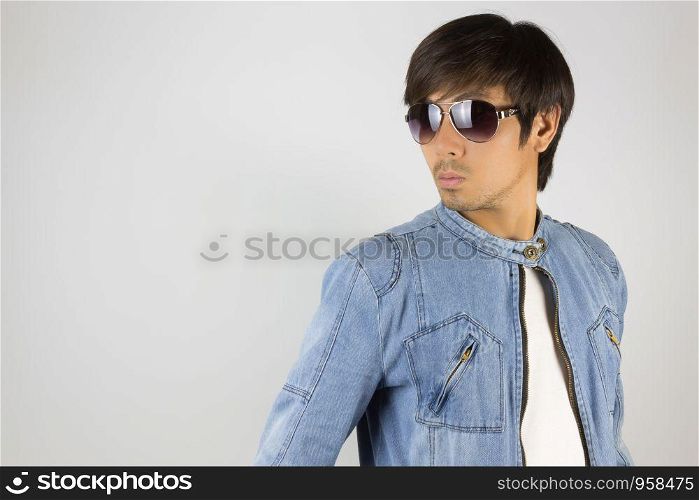 Young Asian Man in Jeans Jacket or Denim Jacket Wear Sunglasses at Right Frame. Denim or Jeans Jacket Men Fashion on Gray Background