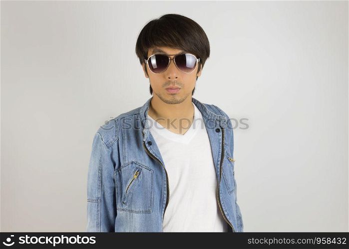 Young Asian Man in Jeans Jacket or Denim Jacket Wear Sunglasses in Front View. Denim or Jeans Jacket Men Fashion on Gray Background