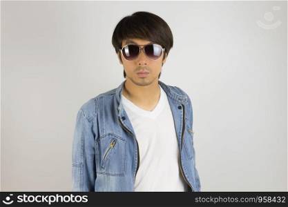 Young Asian Man in Jeans Jacket or Denim Jacket Wear Sunglasses in Front View. Denim or Jeans Jacket Men Fashion on Gray Background
