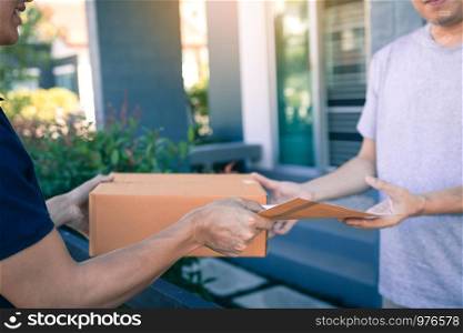 Young asian man smiling while delivering a cardboard box to the woman holding document to signing signature.