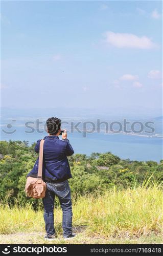 Young Asian man traveler with backpack taking photo on mountains in Thailand.