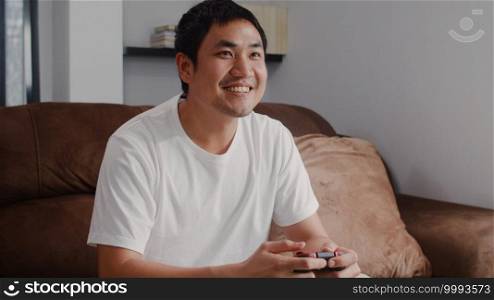 Young Asian man using joystick playing video games in television in living room, male feeling happy using relax time lying on sofa at home. Men play games relax at home concept.