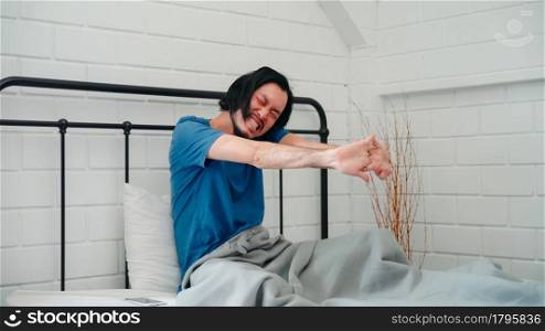 Young Asian man wake up in the morning, male stretching after awake on bed in bedroom at home. Handsome men nap, sleepy relax in modern house concept.