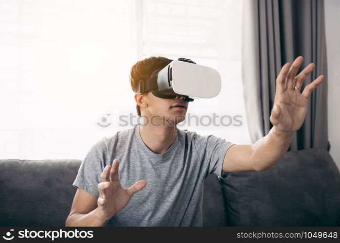 Young asian man wearing virtual reality glasses at living room for admiring virtual reality.