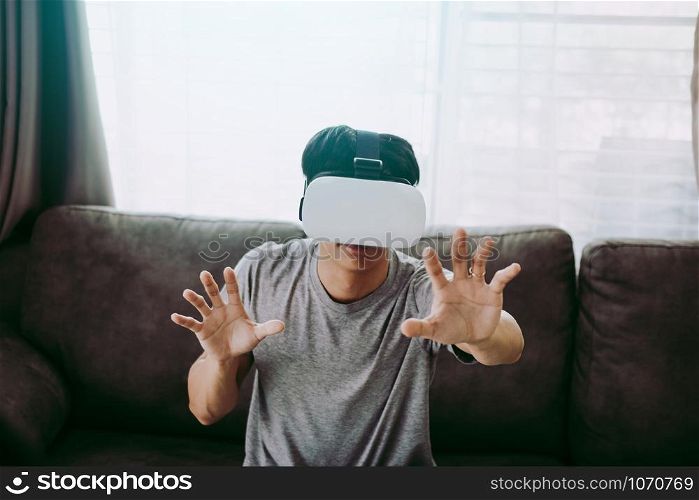 Young asian man wearing virtual reality glasses at living room for admiring virtual reality.