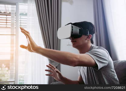 Young asian man wearing virtual reality glasses at living room for admiring virtual reality.