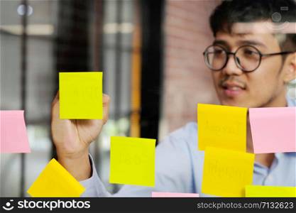 Young asian man writing on sticky note at office, business brainstorming creative ideas, office lifestyle, success in business concept
