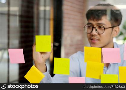 Young asian man writing on sticky note at office, business brainstorming creative ideas, office lifestyle, success in business concept