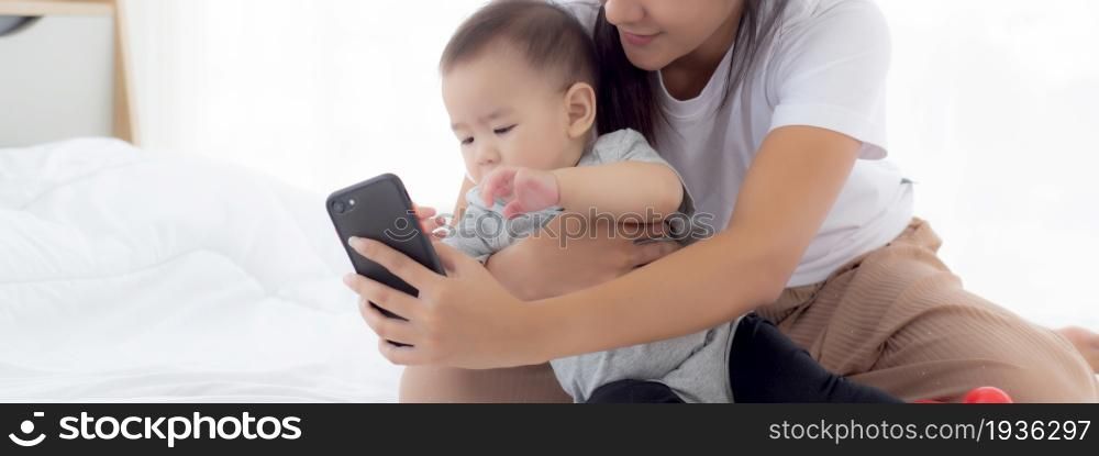 Young asian mother and little baby girl or newborn selfie with smart phone on bed in bedroom, happiness mom and daughter using phone video call at home, two people, family and communication concept.