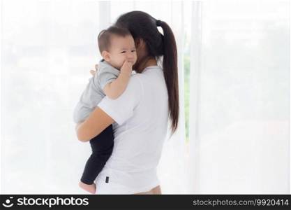 Young asian mother holding little baby girl and walking together in the bedroom at home, mom carry daughter and care, relationship of parent and child, toddler and parent, indoor, family concept.