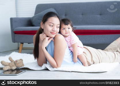 Young Asian mother lying on floor, giving cute 7 month newborn baby girl piggyback ride, enjoying active leisure time. Smiling little infant playing sitting and leaning on mom back. Family bonding