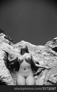 Young Asian nude woman leaning on rock with eyes closed.