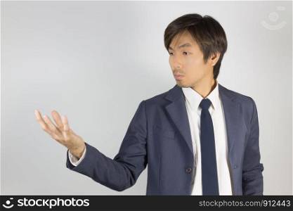 Young Asian Portrait Businessman in Navy Blue Suit Show Hand and Looking Palm of Hand on Grey Background at Right Frame