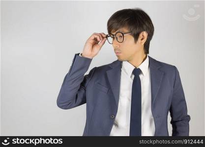 Young Asian Portrait Businessman in Navy Blue Suit Touch Eyeglasses and Look Below on Grey Background