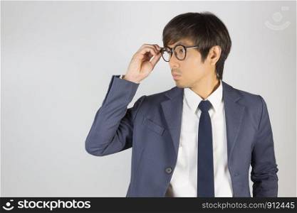Young Asian Portrait Businessman in Navy Blue Suit Touch Eyeglasses and Look Beside on Grey Background