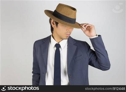 Young Asian Portrait Businessman in Navy Blue Suit Touch Hat Brim and Look Below on Grey Background