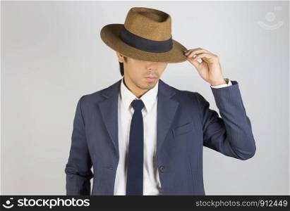 Young Asian Portrait Businessman in Navy Blue Suit Touch Hat Brim at Front View on Grey Background