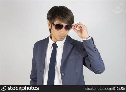 Young Asian Portrait Businessman in Navy Blue Suit Touch Sunglasses and Look Below on Grey Background