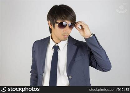 Young Asian Portrait Businessman in Navy Blue Suit Touch Sunglasses and Look Beside on Grey Background