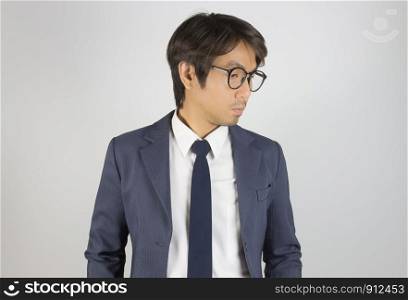 Young Asian Portrait Businessman in Navy Blue Suit Wear Eyeglasses and Look Below on Grey Background