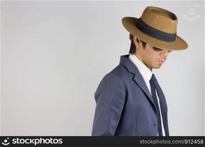 Young Asian Portrait Businessman in Navy Blue Suit Wear Hat and Sunglasses Looking Below at Right Frame on Grey Background