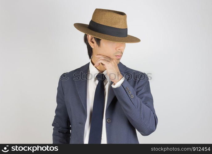 Young Asian Portrait Businessman in Navy Blue Suit Wear Hat and Touch Chin Pose on Grey Background