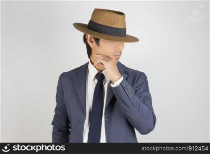 Young Asian Portrait Businessman in Navy Blue Suit Wear Hat and Touch Chin Pose on Grey Background