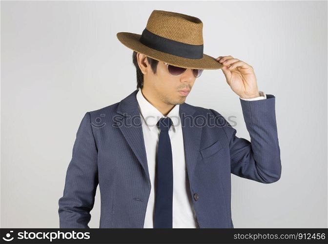Young Asian Portrait Businessman in Navy Blue Suit Wear Sunglasses and Touch Hat Brim at Front View Pose on Grey Background