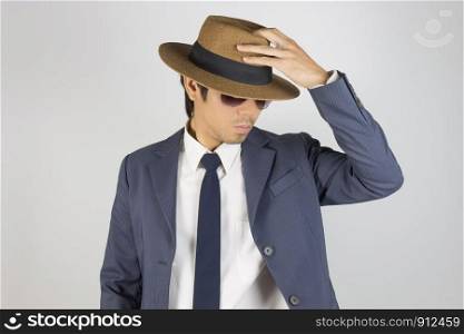 Young Asian Portrait Businessman in Navy Blue Suit Wear Sunglasses and Touch Top of Hat on Grey Background