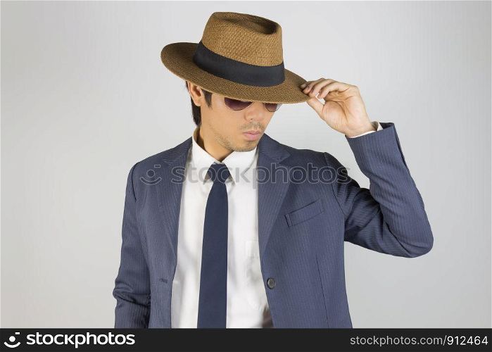 Young Asian Portrait Businessman in Navy Blue Suit Wear Sunglasses and Touch Hat Brim in Front View on Grey Background