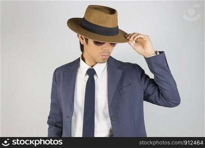 Young Asian Portrait Businessman in Navy Blue Suit Wear Sunglasses and Touch Hat Brim in Front View on Grey Background