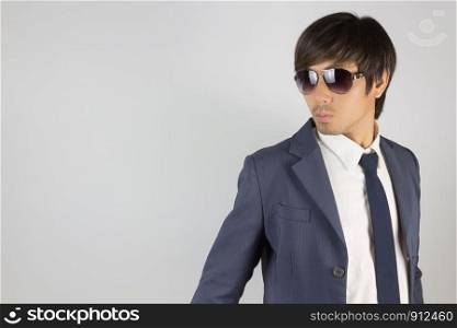 Young Asian Portrait Businessman in Navy Blue Suit Wear Sunglasses and Turn Back Pose at Right Frame on Grey Background