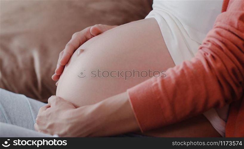 Young Asian Pregnant woman holding her belly talking with her child. Mom feeling happy smiling positive and peaceful while take care baby, pregnancy lying on sofa in living room at home concept.