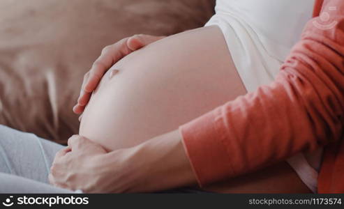 Young Asian Pregnant woman holding her belly talking with her child. Mom feeling happy smiling positive and peaceful while take care baby, pregnancy lying on sofa in living room at home concept.