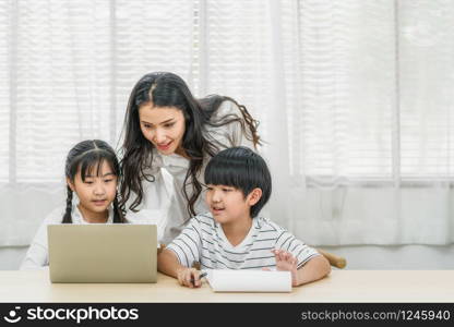 Young Asian Single Mother teaching or helping daughter and son doing home work with technology laptop in home, home school education, relationship and family, communication and conversation concept